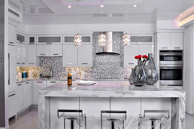 Example of a minimalist porcelain tile and white floor kitchen design in Miami with flat-panel cabinets, white cabinets, metallic backsplash, glass tile backsplash, stainless steel appliances and an island