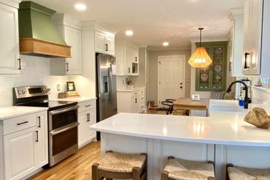 L-shaped medium tone wood floor and brown floor eat-in kitchen photo in Other with a farmhouse sink, white cabinets, quartzite countertops, white backsplash, ceramic backsplash, stainless steel appliances, a peninsula and white countertops