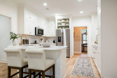 Example of a mid-sized trendy l-shaped light wood floor and brown floor eat-in kitchen design in Atlanta with an undermount sink, beaded inset cabinets, white cabinets, quartz countertops, white backsplash, ceramic backsplash, stainless steel appliances and white countertops