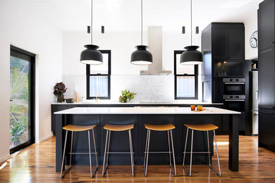 This is an example of a mid-sized transitional single-wall kitchen in Sydney with white splashback, marble splashback, stainless steel appliances, light hardwood floors, with island, brown floor and recessed-panel cabinets.