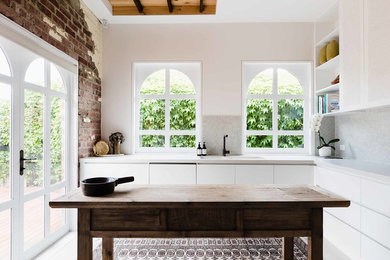 Inspiration for a mediterranean l-shaped separate kitchen in Melbourne with an integrated sink, flat-panel cabinets, white cabinets, beige splashback, mosaic tile splashback, panelled appliances, with island, beige floor and beige benchtop.