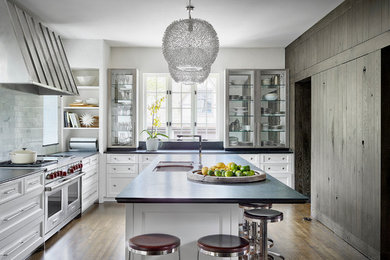 This is an example of a country l-shaped kitchen in Chicago with an undermount sink, recessed-panel cabinets, white cabinets, white splashback, stainless steel appliances, dark hardwood floors and with island.