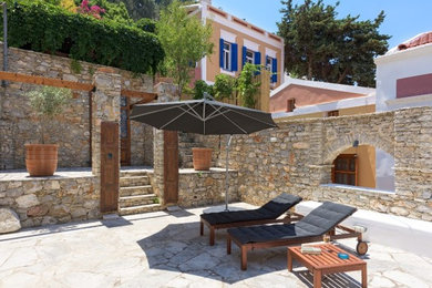 他の地域にある巨大な地中海スタイルのおしゃれな裏庭のテラス (屋外シャワー、天然石敷き、オーニング・日よけ) の写真