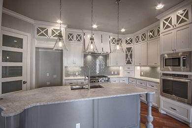 Kitchen pantry - modern l-shaped medium tone wood floor kitchen pantry idea in Oklahoma City with a farmhouse sink, glass-front cabinets, white cabinets, marble countertops, gray backsplash, glass tile backsplash, stainless steel appliances and an island