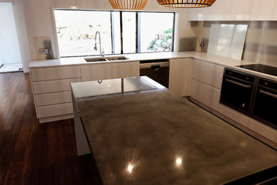 Inspiration for a contemporary l-shaped eat-in kitchen in Sydney with an undermount sink, flat-panel cabinets, white cabinets, concrete benchtops, white splashback, ceramic splashback, stainless steel appliances, medium hardwood floors and with island.