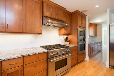 Large elegant u-shaped light wood floor and brown floor eat-in kitchen photo in Vancouver with a double-bowl sink, shaker cabinets, medium tone wood cabinets, granite countertops, white backsplash, subway tile backsplash, stainless steel appliances and an island