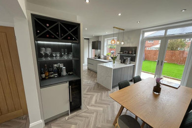 Photo of a medium sized modern grey and black l-shaped kitchen/diner in Other with a built-in sink, flat-panel cabinets, grey cabinets, quartz worktops, white splashback, stone slab splashback, integrated appliances, vinyl flooring, a breakfast bar, grey floors, white worktops and feature lighting.