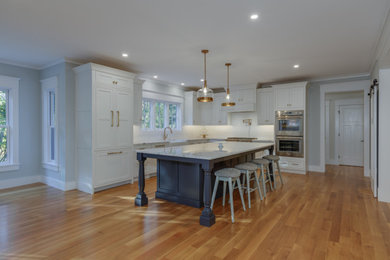Kitchen - large l-shaped medium tone wood floor kitchen idea in Boston with a farmhouse sink, shaker cabinets, white cabinets, white backsplash, subway tile backsplash, stainless steel appliances and an island