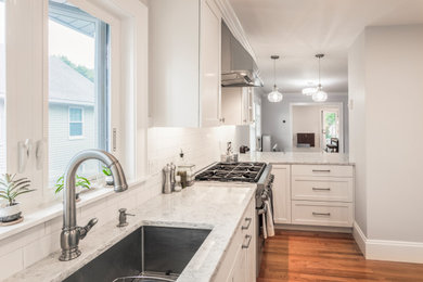 Trendy u-shaped medium tone wood floor eat-in kitchen photo in Boston with an undermount sink, recessed-panel cabinets, white cabinets, granite countertops, white backsplash, subway tile backsplash, stainless steel appliances and a peninsula