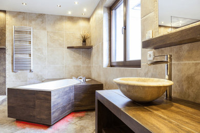 Example of a large trendy master beige tile and porcelain tile porcelain tile, beige floor, single-sink and vaulted ceiling freestanding bathtub design in Los Angeles with furniture-like cabinets, medium tone wood cabinets, a two-piece toilet, beige walls, a vessel sink, wood countertops, brown countertops and a built-in vanity