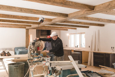 Example of a mid-sized classic enclosed medium tone wood floor and exposed beam living room design in Other with white walls, a wood stove, a stone fireplace and no tv