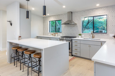 Example of a trendy l-shaped light wood floor and beige floor kitchen design in Austin with a single-bowl sink, flat-panel cabinets, gray cabinets, multicolored backsplash, stainless steel appliances, a peninsula and white countertops