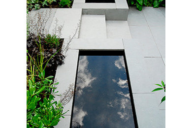 This is an example of a mid-sized contemporary partial sun backyard stone water fountain landscape in London for summer.