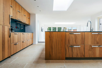 Design ideas for a large contemporary galley kitchen in Cambridgeshire with flat-panel cabinets, dark wood cabinets, solid surface benchtops, black splashback, stainless steel appliances, limestone floors, with island, beige floor and black benchtop.