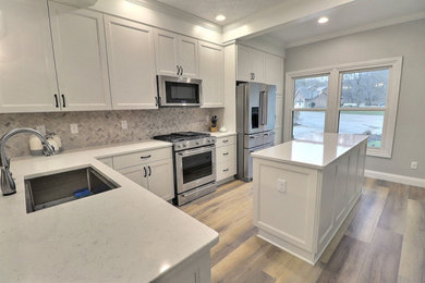 Example of a mid-sized transitional l-shaped vinyl floor and beige floor eat-in kitchen design in Other with an undermount sink, shaker cabinets, white cabinets, quartz countertops, white backsplash, limestone backsplash, stainless steel appliances, an island and white countertops