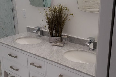 This is an example of a large contemporary master bathroom in Toronto with flat-panel cabinets, white cabinets, a freestanding tub, a double shower, a two-piece toilet, white tile, stone tile, white walls, ceramic floors, an undermount sink and marble benchtops.