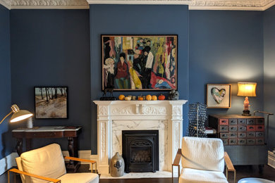 Cette image montre un grand salon traditionnel fermé avec un mur bleu, parquet foncé, une cheminée standard, un manteau de cheminée en pierre et un sol marron.