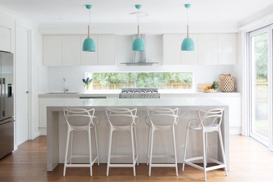 Photo of a mid-sized beach style galley eat-in kitchen in Sydney with an undermount sink, white cabinets, quartz benchtops, white splashback, subway tile splashback, stainless steel appliances, medium hardwood floors, with island, brown floor and grey benchtop.