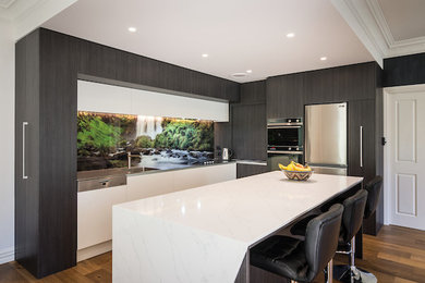 Design ideas for a mid-sized galley eat-in kitchen in Christchurch with a drop-in sink, flat-panel cabinets, grey cabinets, solid surface benchtops, multi-coloured splashback, glass sheet splashback, stainless steel appliances, medium hardwood floors, with island, brown floor and white benchtop.