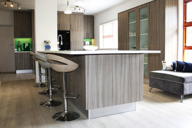 Example of a mid-sized minimalist light wood floor enclosed kitchen design in Other with a single-bowl sink, flat-panel cabinets, light wood cabinets, solid surface countertops, blue backsplash, glass tile backsplash, stainless steel appliances and an island