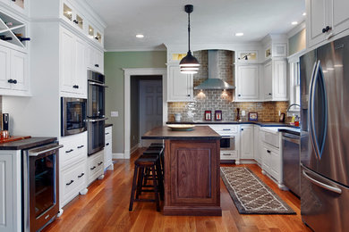 Inspiration for a mid-sized timeless u-shaped medium tone wood floor and brown floor enclosed kitchen remodel in Providence with a farmhouse sink, raised-panel cabinets, white cabinets, gray backsplash, subway tile backsplash, stainless steel appliances and an island