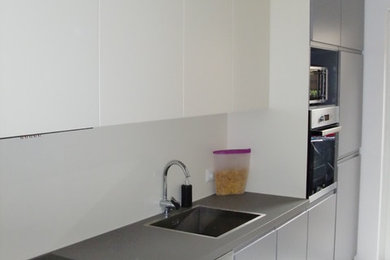 Photo of a mid-sized contemporary single-wall separate kitchen in Dusseldorf with an integrated sink, flat-panel cabinets, grey cabinets, wood benchtops, beige splashback, black appliances, ceramic floors and no island.