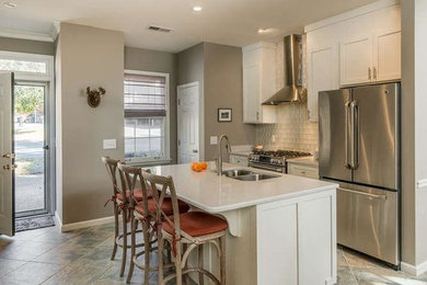Photo of a medium sized traditional single-wall open plan kitchen in Nashville with a double-bowl sink, recessed-panel cabinets, white cabinets, engineered stone countertops, white splashback, glass tiled splashback, stainless steel appliances, slate flooring, an island, beige floors and white worktops.