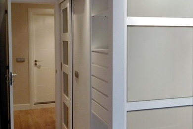Diseño de armario vestidor unisex actual de tamaño medio con puertas de armario blancas y suelo de madera en tonos medios