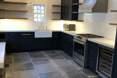 Photo of a large country u-shaped eat-in kitchen in New York with a farmhouse sink, shaker cabinets, black cabinets, quartz benchtops, white splashback, porcelain splashback, panelled appliances, grey floor and grey benchtop.