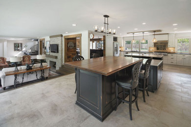 Example of a huge beach style u-shaped travertine floor and beige floor open concept kitchen design in Columbus with raised-panel cabinets, distressed cabinets, wood countertops, two islands and brown countertops