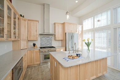 Design ideas for a mid-sized transitional l-shaped eat-in kitchen in DC Metro with a farmhouse sink, shaker cabinets, light wood cabinets, quartz benchtops, blue splashback, subway tile splashback, stainless steel appliances, porcelain floors, with island, brown floor and grey benchtop.