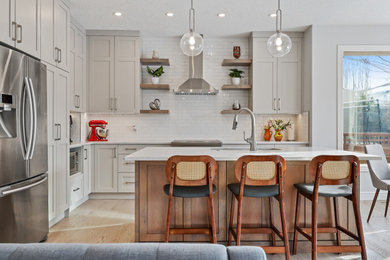 Inspiration for a mid-sized contemporary l-shaped light wood floor and brown floor open concept kitchen remodel in Calgary with an undermount sink, shaker cabinets, gray cabinets, quartz countertops, white backsplash, ceramic backsplash, stainless steel appliances, an island and white countertops
