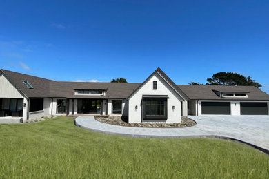 This is an example of an expansive contemporary one-storey brick beige house exterior in Auckland with a gable roof, a shingle roof, a brown roof and board and batten siding.