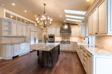 Example of a l-shaped medium tone wood floor, brown floor and vaulted ceiling eat-in kitchen design in Other with an undermount sink, white cabinets, granite countertops, beige backsplash, ceramic backsplash, stainless steel appliances, an island and beige countertops