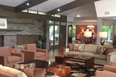 Huge 1950s open concept medium tone wood floor and brown floor living room photo in Other with beige walls, a stone fireplace, a standard fireplace and a bar