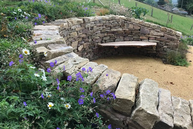 This is an example of a medium sized rustic sloped full sun garden in Cheshire with a retaining wall and gravel.