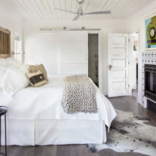 Landhaus Schlafzimmer mit weißer Wandfarbe, dunklem Holzboden, gefliester Kaminumrandung, Gaskamin und braunem Boden in Sonstige