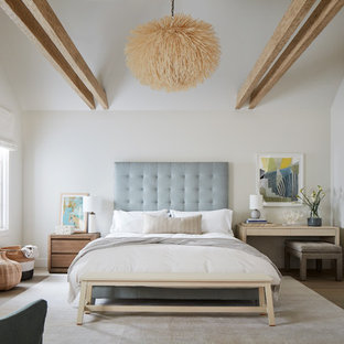 This is an example of a large beach style master bedroom in San Luis Obispo with white walls, a standard fireplace, medium hardwood floors, a wood fireplace surround and brown floor.