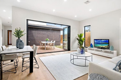 This is an example of a mid-sized contemporary open concept living room in Melbourne with white walls, light hardwood floors, a freestanding tv and beige floor.