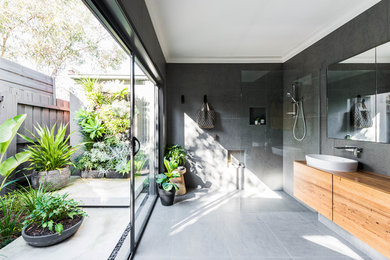 This is an example of a large contemporary master bathroom in Melbourne with flat-panel cabinets, brown cabinets, a curbless shower, gray tile, grey walls, a vessel sink, wood benchtops, grey floor, an open shower and brown benchtops.