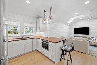 Kitchen - small coastal u-shaped light wood floor and vaulted ceiling kitchen idea in Other with an undermount sink, shaker cabinets, white cabinets, wood countertops, stainless steel appliances and brown countertops