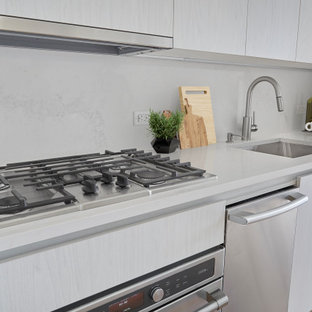 Imagen de cocina comedor lineal, industrial, pequeña, con fregadero encastrado, armarios con paneles lisos, puertas de armario de madera clara, encimera de mármol, salpicadero blanco, electrodomésticos de acero inoxidable, suelo de madera clara, una isla, suelo beige y encimeras blancas