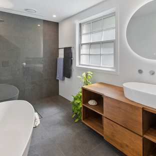 Mid-sized contemporary master bathroom in Sydney with a freestanding tub, porcelain tile, white walls, porcelain floors, a vessel sink, wood benchtops, grey floor, an open shower, flat-panel cabinets, medium wood cabinets, a curbless shower, gray tile and brown benchtops.