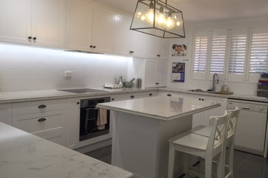 Large transitional u-shaped eat-in kitchen in Brisbane with a double-bowl sink, raised-panel cabinets, white cabinets, quartz benchtops, white splashback, ceramic splashback, stainless steel appliances, porcelain floors and with island.