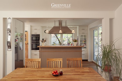 Landhaus Küche mit profilierten Schrankfronten, weißen Schränken, Arbeitsplatte aus Holz, hellem Holzboden und Kücheninsel in Sonstige