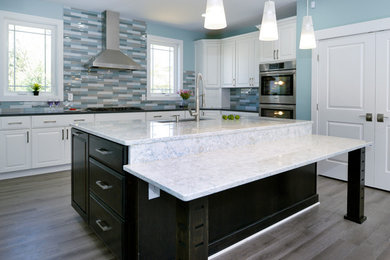 Example of a mid-sized classic u-shaped dark wood floor kitchen design in Orange County with a farmhouse sink, raised-panel cabinets, white cabinets, multicolored backsplash, glass tile backsplash and an island