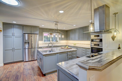 Example of a mid-sized transitional u-shaped laminate floor and brown floor eat-in kitchen design in Seattle with a drop-in sink, recessed-panel cabinets, laminate countertops, multicolored backsplash, stainless steel appliances, an island, multicolored countertops, ceramic backsplash and gray cabinets