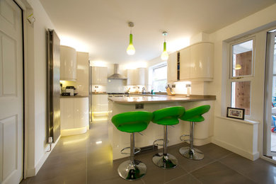This is an example of a medium sized contemporary u-shaped open plan kitchen in Cardiff with a double-bowl sink, flat-panel cabinets, white cabinets, composite countertops, stainless steel appliances, porcelain flooring, a breakfast bar and grey floors.