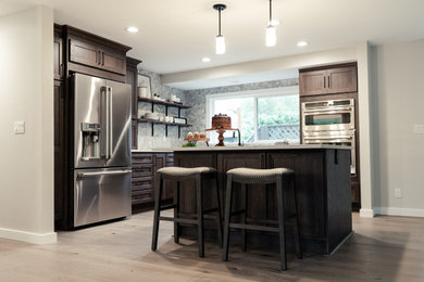 Example of a mid-sized transitional l-shaped light wood floor eat-in kitchen design in Seattle with an undermount sink, shaker cabinets, dark wood cabinets, quartz countertops, white backsplash, marble backsplash, stainless steel appliances, an island and white countertops