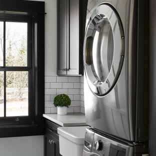 Esempio di una piccola sala lavanderia contemporanea con lavello stile country, ante in stile shaker, ante nere, top in quarzo composito, paraspruzzi bianco, paraspruzzi con piastrelle in ceramica, pareti bianche, pavimento in cemento, lavatrice e asciugatrice a colonna, top grigio e pannellatura